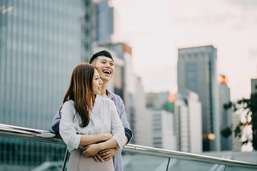 Loving couple embracing and laughing joyfully against modern cityscape over urban terrace