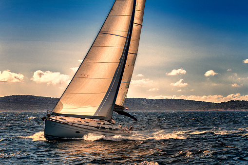 Sailing boat moving gracefully on wavy blue sea between scenic Croatian Islands. Sailboat with the wind in unfurled white sails on an adventurous summer voyage along the picturesque Adriatic coastline