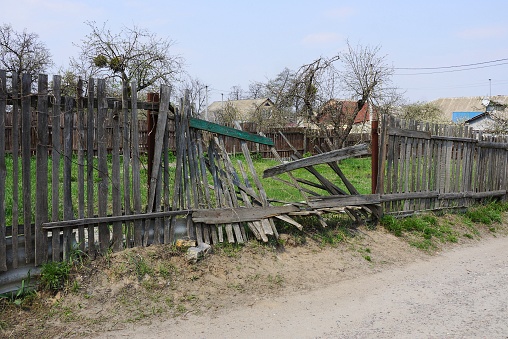 old gray broken wooden plank fence in green grass on a rural street