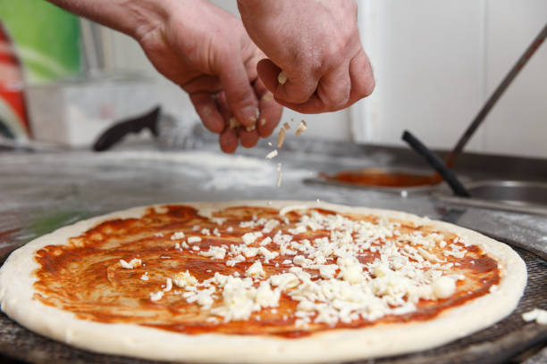 The hands of chef sprinkles the pizza with cheese in restaurant kitchen