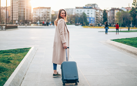 Young woman walking on a sidewalk and pulling a small wheeled luggage