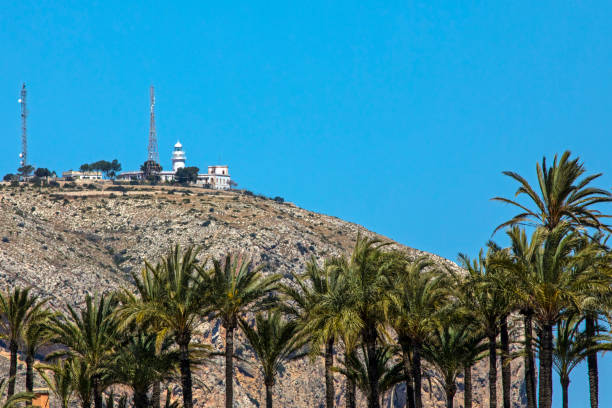 A view above the palm trees of the lighthouse and cliffs of Cap de Sant Antoni in Javea, Spain.