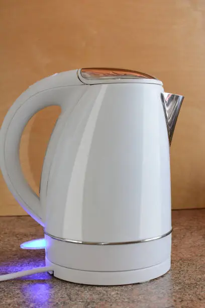 the switched-on electric kettle on a table against the background of a wooden board