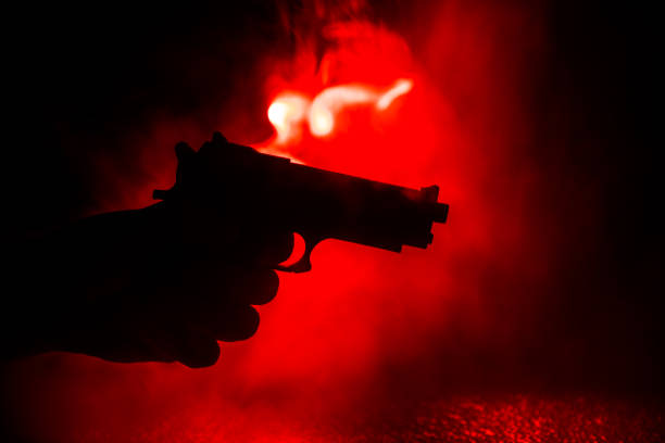 istock Male hand holding gun on black background with smoke toned back lights 1145703215