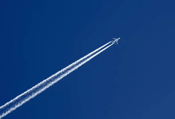 Aeroplane in the clear blue sky leaving vapor trails behind