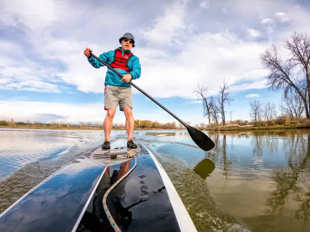athletic senior man on a stand up paddleboard on  a calm lake in Colorado, bow view