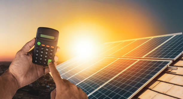 Holding a calculator on a solar panel photovoltaic installation in the background. stock photo