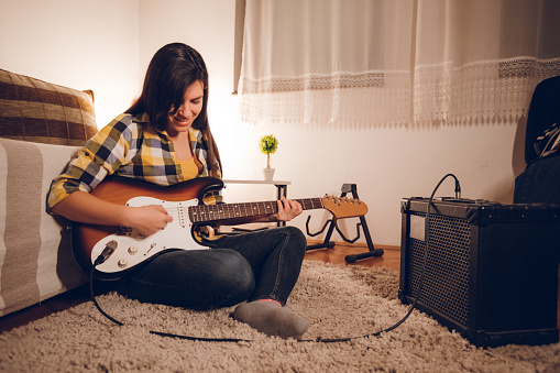 Young caucasian woman playing the electric guitar, at home, sitting on the floor.