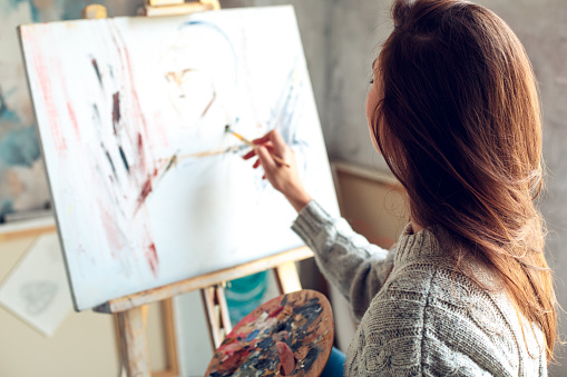 Young woman artist painting at home sitting drawing abstract picture in process back view concentrated close-up
