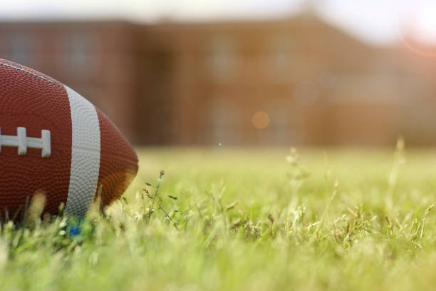 Football on grass stadium on college or high school campus. School building in background.  No people.  Daytime.