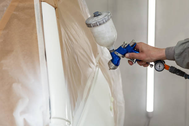 A male worker paints with a spray gun a part of the car body in white after being damaged at an accident. Door from the vehicle during the repair in the workshop. Auto service industry professions un trabajador masculino pinta con una pistola pulverizadora una parte del cuerpo del automóvil en blanco después de sufrir daños en un accidente. puerta del vehículo durante la reparación en el taller. las profesiones del sector de servicios automáti