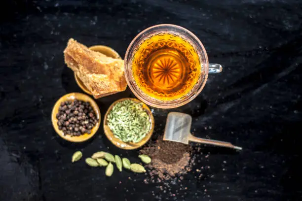 Close up of popular type of tea on wooden surface earlier dunked a lot i.e. Jaggery tea with ingredients like fennel,jaggery or gud,black pepper,tea leaves, milk, and green cardamom.