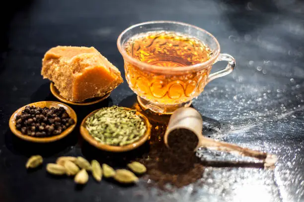 Close up of popular type of tea on wooden surface earlier dunked a lot i.e. Jaggery tea with ingredients like fennel,jaggery or gud,black pepper,tea leaves, milk, and green cardamom.