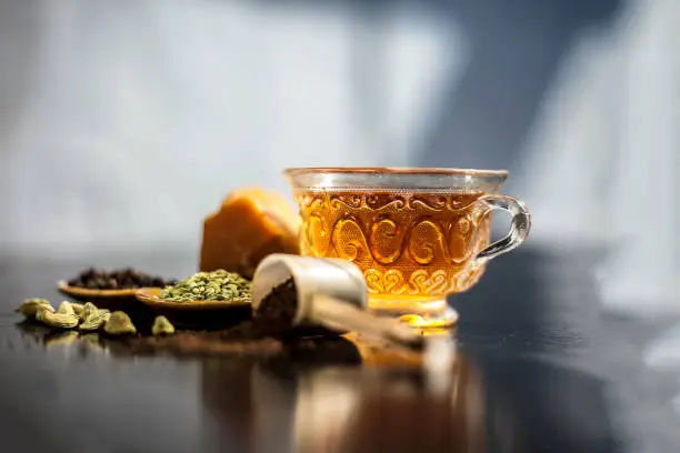 Photo of Close up of popular type of tea on wooden surface earlier dunked a lot i.e. Jaggery tea with ingredients like fennel,jaggery or gud,black pepper,tea leaves, milk, and green cardamom.