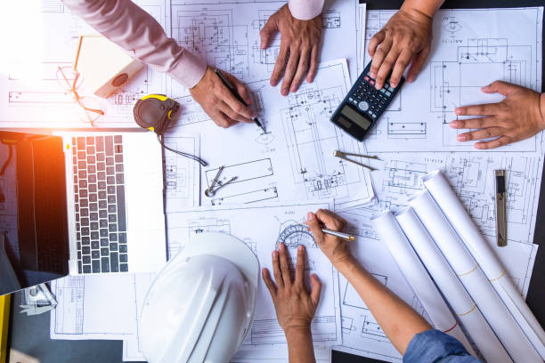 istock engineers pointing to building on blueprint and using laptop to drawing design building Project in office, construction concept. Engineer concept 1145738866