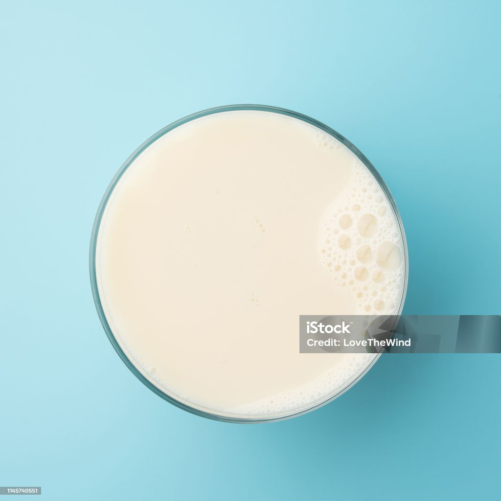 Cup glass with milk or soya soy bean bubble foam on top view isolated t on blue background food drink object design Milk Stock Photo