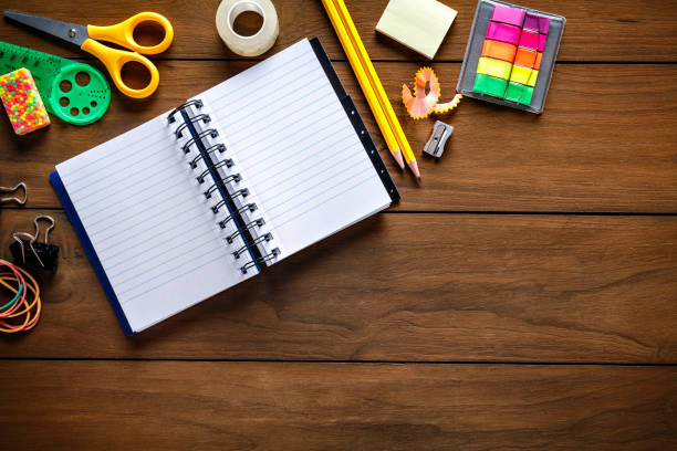 Overhead shot of stationery on wood desk with paper notepad and frame of school office supplies Back to school themes. Overhead shot of stationery on wood desk with paper notepad and frame of school office supplies stapled paper stock pictures, royalty-free photos & images