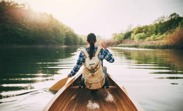 Girl enjoy canoeing Rear view of hipster girl paddling the canoe on the sunset lake. kayaking stock pictures, royalty-free photos & images