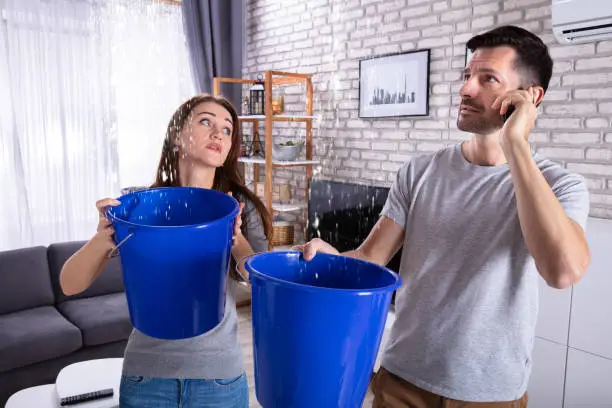 Photo of Couple Using Bucket For Collecting Water Leakage From Ceiling