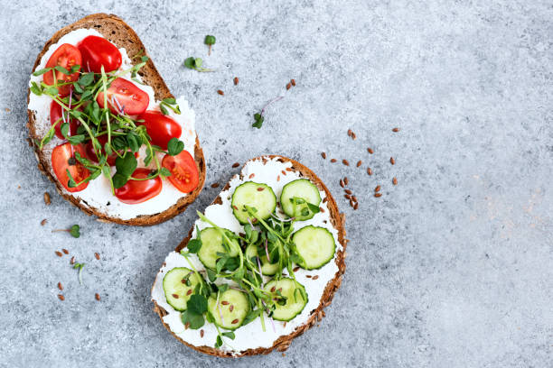 Healthy vegetarian toasts with cream cheese, vegetables, greens Healthy vegetarian toasts with cream cheese, cucumber, cherry tomato and micro greens on top. Table top view on concrete backdrop. Copy space cream cheese stock pictures, royalty-free photos & images