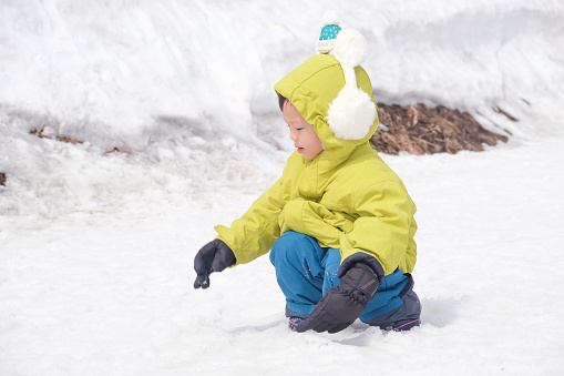 Cute little Asian 2 - 3 years old toddler baby boy child wearing earmuff, snow gloves playing happily in snow, Family travel, Relax and fun winter vacation with child, winter season, Selective focus