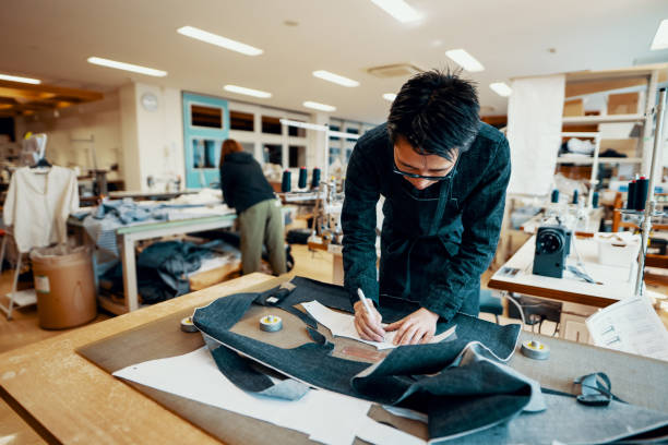 Mid adult tailor cutting denim around a pattern in preparation to make a pair of jeans Mid adult tailor cutting denim around a pattern in preparation to make a pair of jeans by hand in Japan okayama prefecture stock pictures, royalty-free photos & images