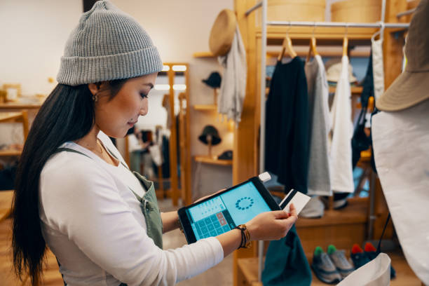 Retail shop clerk taking a mobile credit card payment on a digital tablet Retail shop clerk taking a mobile credit card payment on a digital tablet in a clothing boutique in Japan clothing store credit card stock pictures, royalty-free photos & images