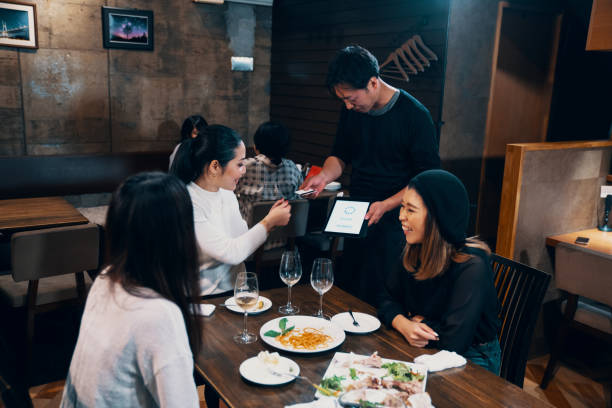 istock Three mid adult women a meal at a restaurant using mobile payment on a digital tablet 1145786408