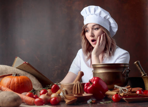 istock Surprised woman in a chef's uniform reads an old cookbook. 1145788187