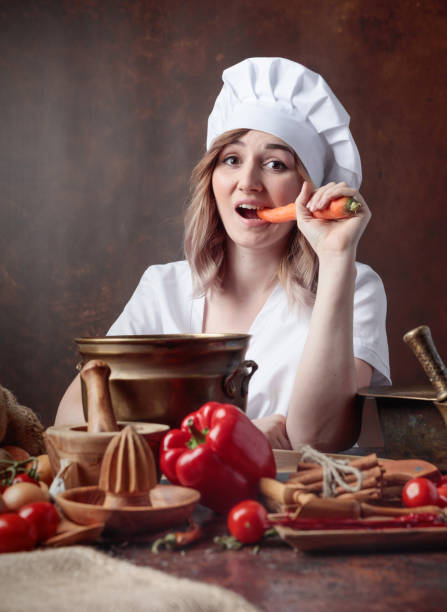 istock Young woman in a chef's uniform eating carrots. 1145788188