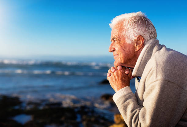 A good-looking silver haired man sits contentedly next to the sea in the sunshine, smiling and enjoying his retirement.