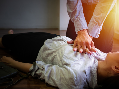 hombre de oficina voluntario usar bomba de mano en el pecho para la RCP de emergencia de primeros auxilios en la mujer de ataque cardíaco inconsciente, tratar de resucitación mujer paciente en el trabajo photo