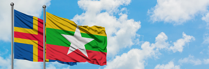 Aland Islands and Myanmar flag waving in the wind against white cloudy blue sky together. Diplomacy concept, international relations.