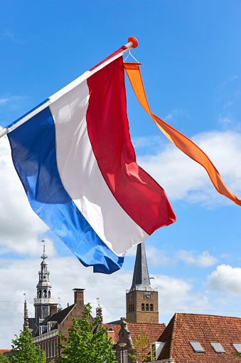 Dutch flag with orange streamer waving in the wind agains a blue sky with white clouds and cityscape of Franeker the Netherlands on Koningsdag. A national holiday in the Kingdom of the Netherlands
