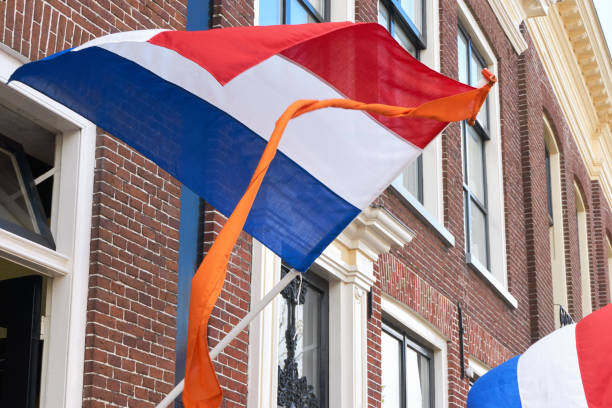 Dutch flags with orange streamer waving in the wind on facades of typical dutch houses on Koningsdag or King's day in the Netherlands. A national holiday in the Kingdom of the Netherlands.