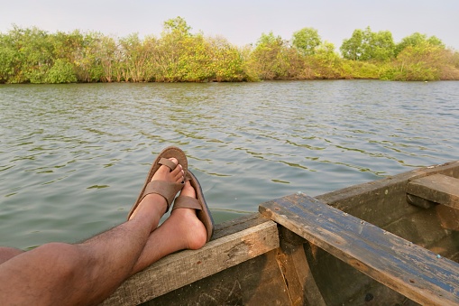 Image of feet resting on wooden canoe travelling through the Kerala Backwaters, India. A popular tourism activity for visitors to the mangrove habitat.