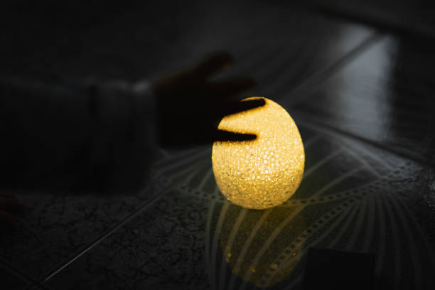 Light golden Easter egg on the floor with blur baby hand on dark background. Happy Easter concept.