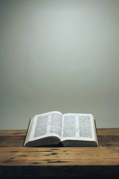 Open Holy Bible on a old oak wooden table.  Grey wall background.
