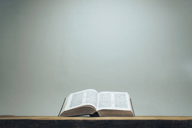 istock Open Holy Bible on a old oak wooden table.  Grey wall background. 1145812806