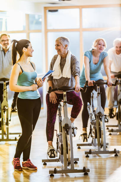 glückliche reife frau im gespräch mit ihrem trainer während der spinnklasse im health club. - spinning instructor exercising gym stock-fotos und bilder