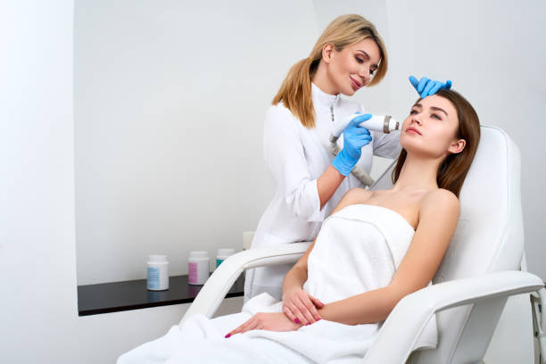 Pretty blonde beautician doctor doing rf-lifting procedure for woman laying in a beauty salon. Hardware cosmetology. Patient receiving electric facial massage. Skin rejuvenation and wrinkle smoothing stock photo