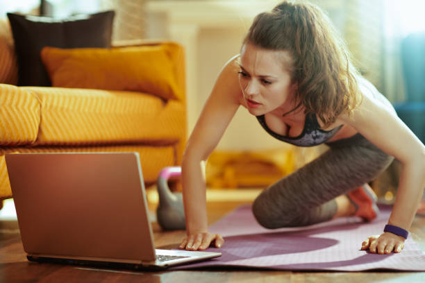 istock woman watching fitness tutorial on internet and doing exercises 1145815598