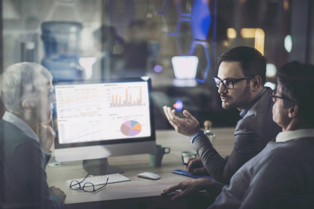 istock Business colleagues talking about charts while working on desktop PC at dark office. 1145816888