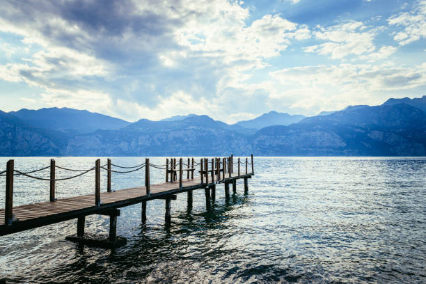 istock Summer holiday: Wooden dock pier over blue lake water. Cloudy evening scenery. 1145821327