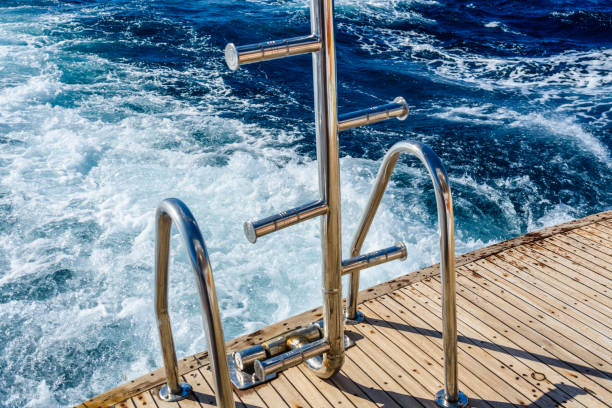 istock Metal staircase for descent into the water and wave trace with white foam on a water surface behind of fast moving yacht 1145833014