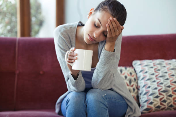 istock Depressed young woman having headache while drinking coffee on sofa at home. 1145837697