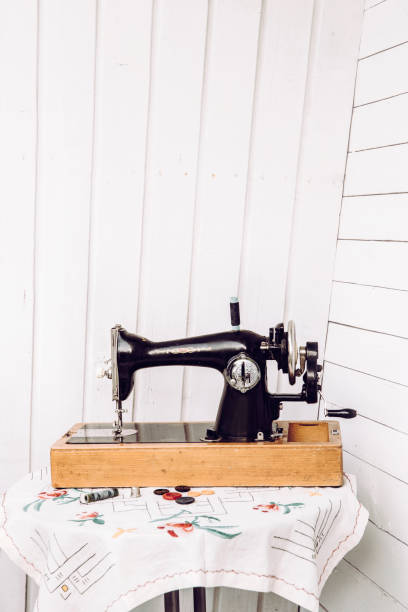 istock Side view of old cool manual sewing machine hand tool with crank on white wooden board background on table. Vintage arts and crafts concepts. 1145838144