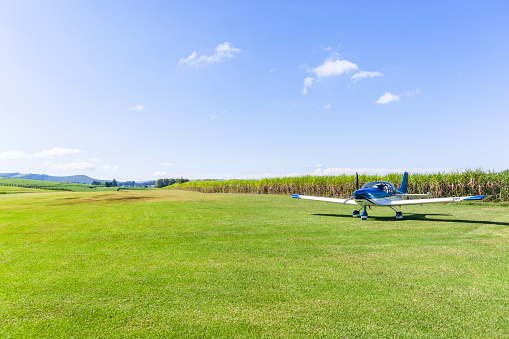 Light single prop aircraft plane parked on rural countryside farm grass airstrip runway between agriculture crops.
