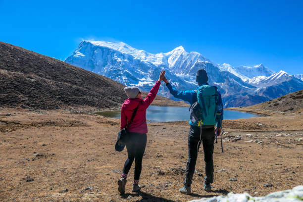Nepal - Couple and the view on Annapurna ChainNepal A couple dancing on the Annapurna Circuit Trek, Himalayas, Nepal. Annapurna chain in the back, covered with snow. Clear weather, dry grass, snowy peaks. High altitude, holding hand up. annapurna circuit photos stock pictures, royalty-free photos & images