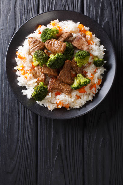 porción de carne de res frita con brócoli con arroz de guarnición y caqui de cerca en un plato. vista superior vertical - beef rice orange stir fried fotografías e imágenes de stock